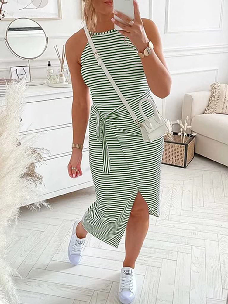 Woman showcasing a green and white striped halter neck dress with a tie waist and side slit, accessorized with white sneakers and a white crossbody bag.