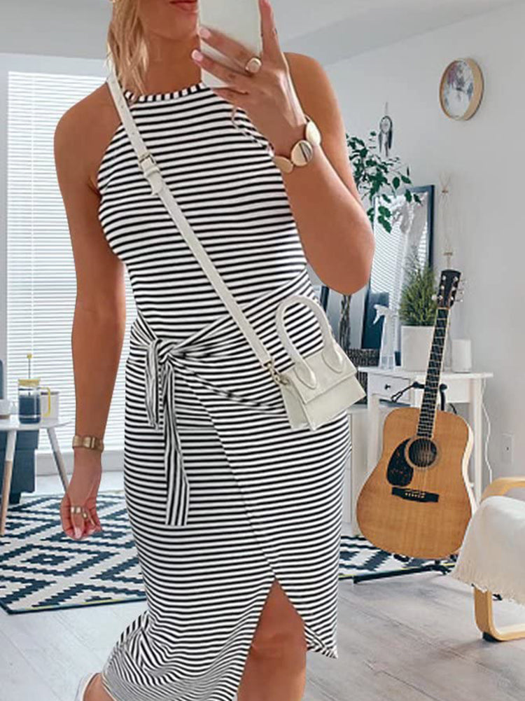 Woman in a black and white striped halter neck dress with a tie waist and side slit, holding a phone and wearing white sneakers and a white crossbody bag.