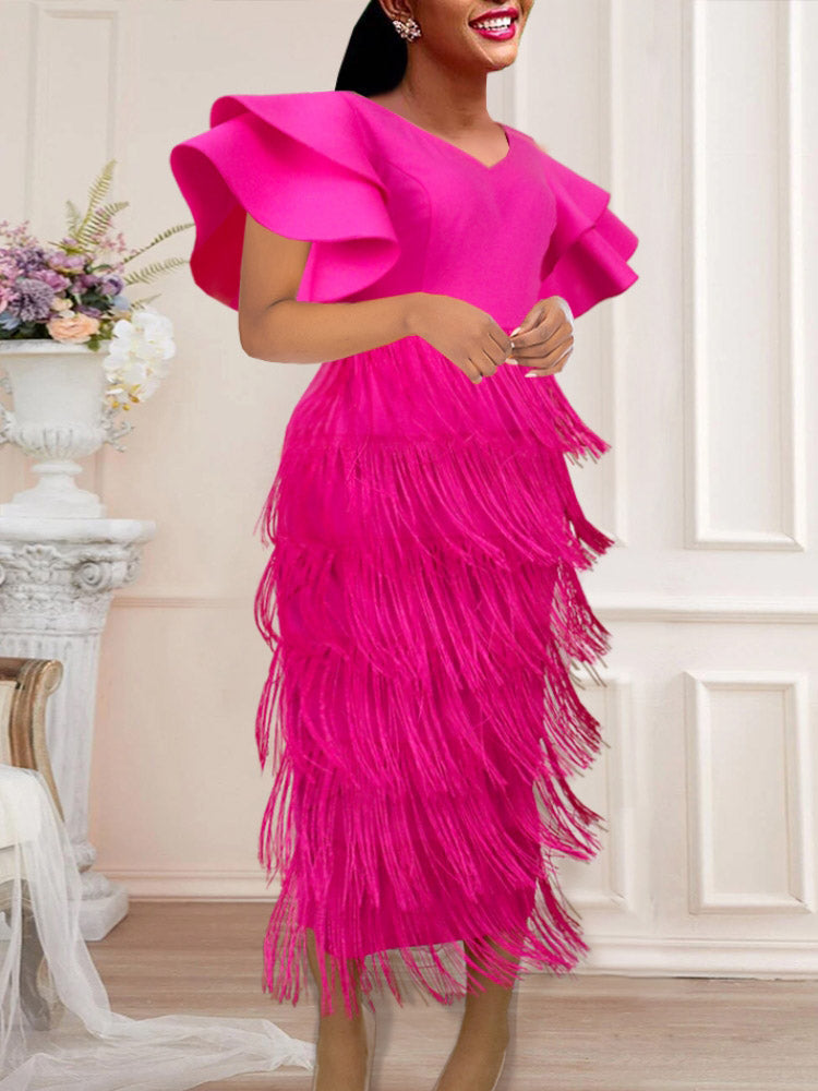 Close-up of a woman in a bright pink fringe dress with dramatic ruffled sleeves, standing in an elegant interior setting.
