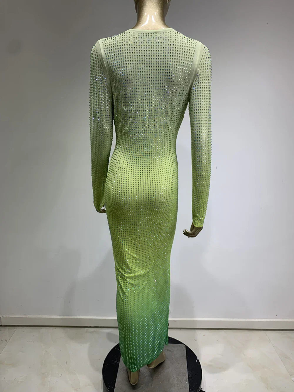 Back view of a mannequin wearing a long, gradient green rhinestone-embellished dress with long sleeves.