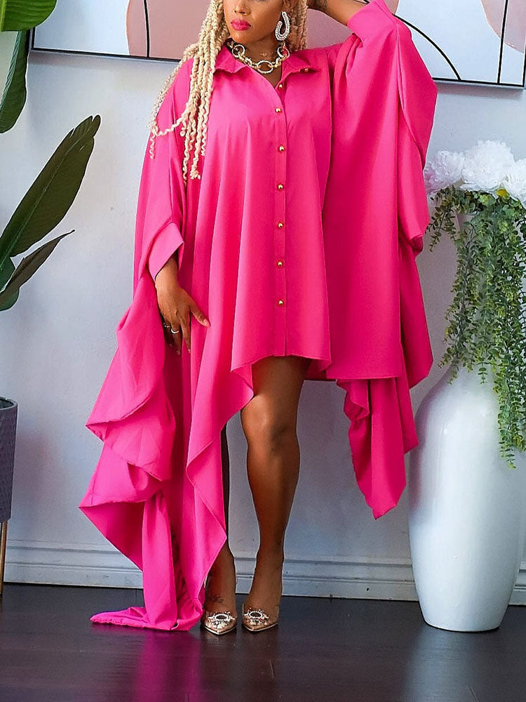Woman wearing a vibrant pink oversized shirt dress with a dramatic asymmetrical hemline and flowing draped layers, paired with clear heels.