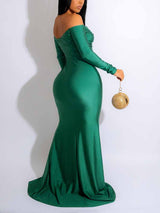 Back view of a woman in a floor-length emerald green off-the-shoulder gown.