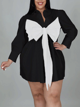 Plus-size woman wearing a black shirt dress with a white oversized bow detail on the front.