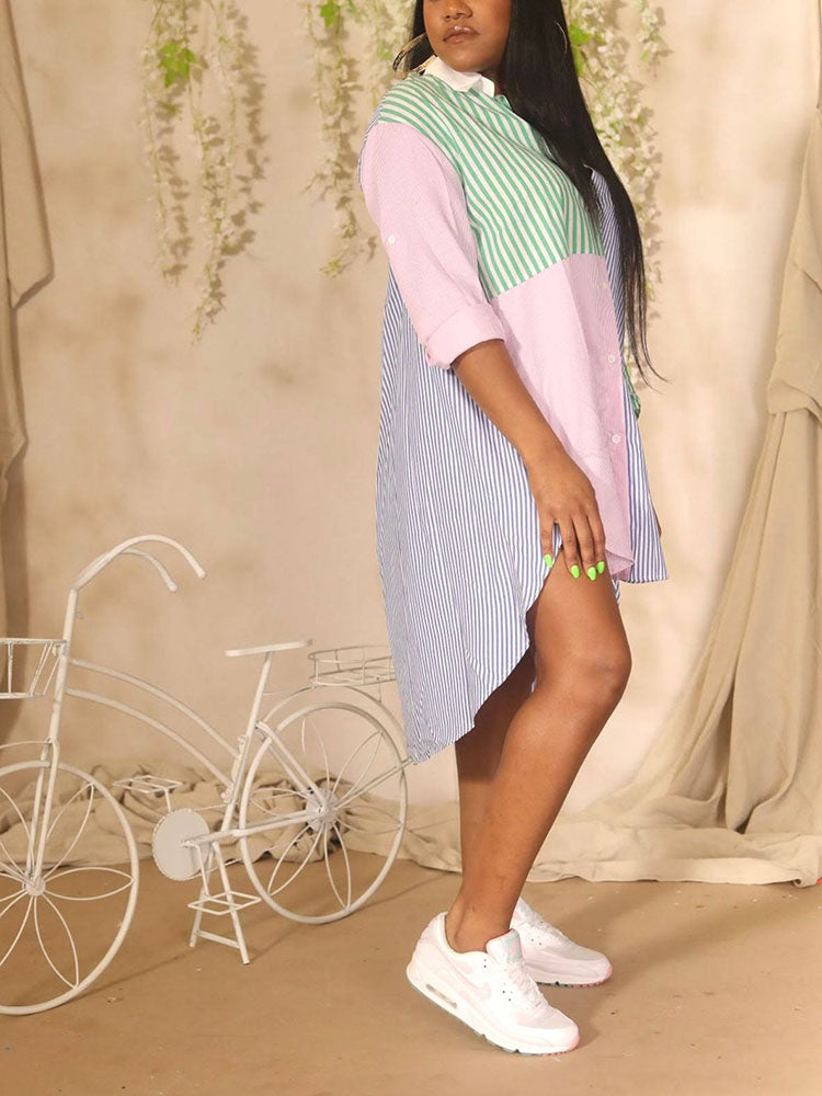 Side view of a woman wearing a colorblock striped button-down shirt dress with a high-low hem and white sneakers, with a decorative bicycle in the background.