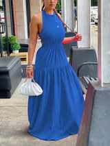 Side view of a woman in a blue halter neck maxi dress with an elasticated waist and tiered skirt.