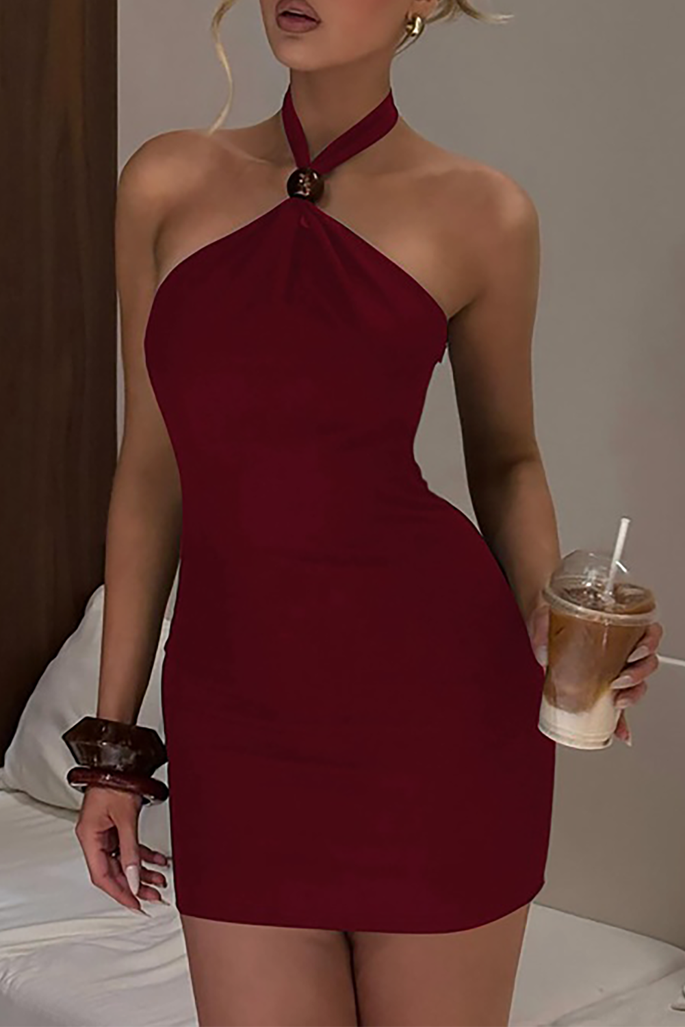 Woman in a maroon halter neck mini dress holding a coffee drink.
