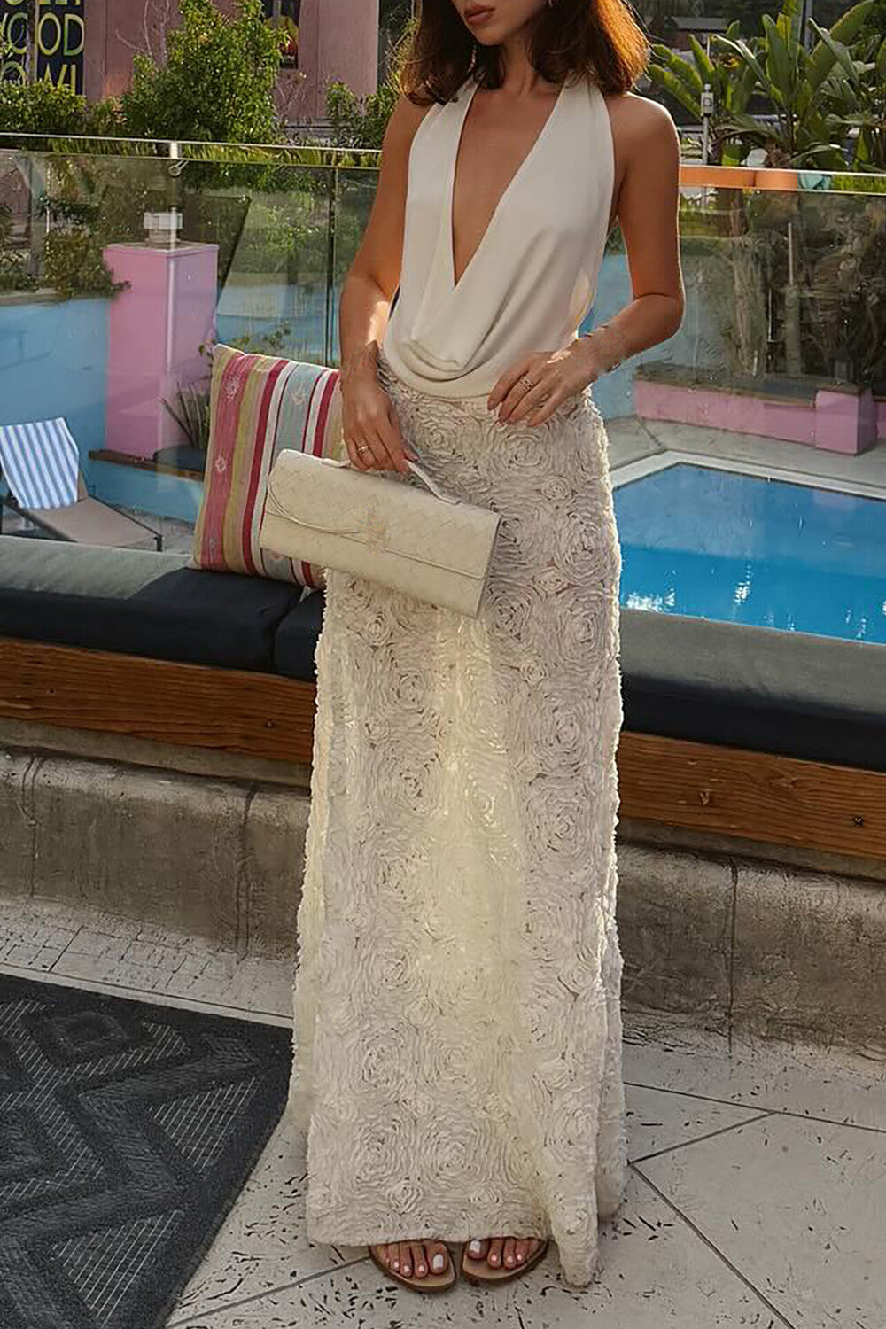 Woman posing by a pool wearing a white halter neck top and a sheer white maxi skirt with rose appliqué