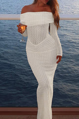 Woman wearing a white off-the-shoulder maxi dress with long sleeves and a textured knit overlay, holding a glass of champagne by the water.