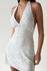 Close-up of a woman wearing a white halter neck mini dress with black polka dots, showing the neckline and bodice.