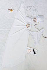 Flat lay of a white one-shoulder maxi dress with a matching bikini set and accessories.