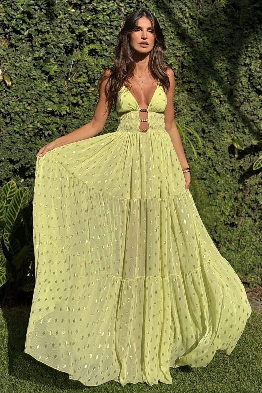 Woman wearing a lime green maxi dress with gold polka dots and a plunging neckline, standing outdoors.