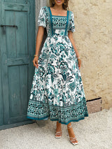 Front view of a woman wearing a white midi dress with a green floral print, square neckline, and short puff sleeves.