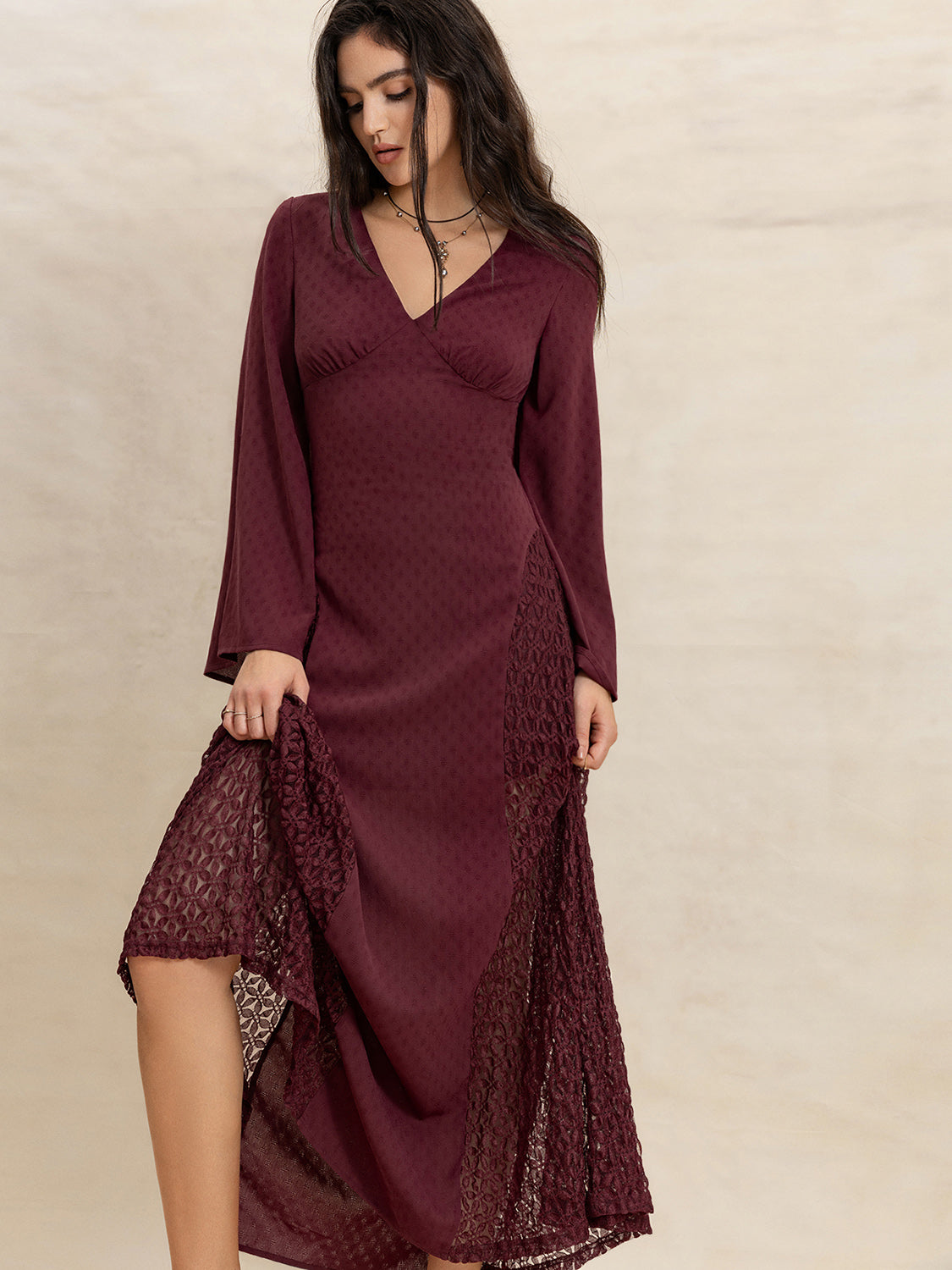 Close-up of a woman lifting the hem of a burgundy maxi dress to reveal lace inserts.