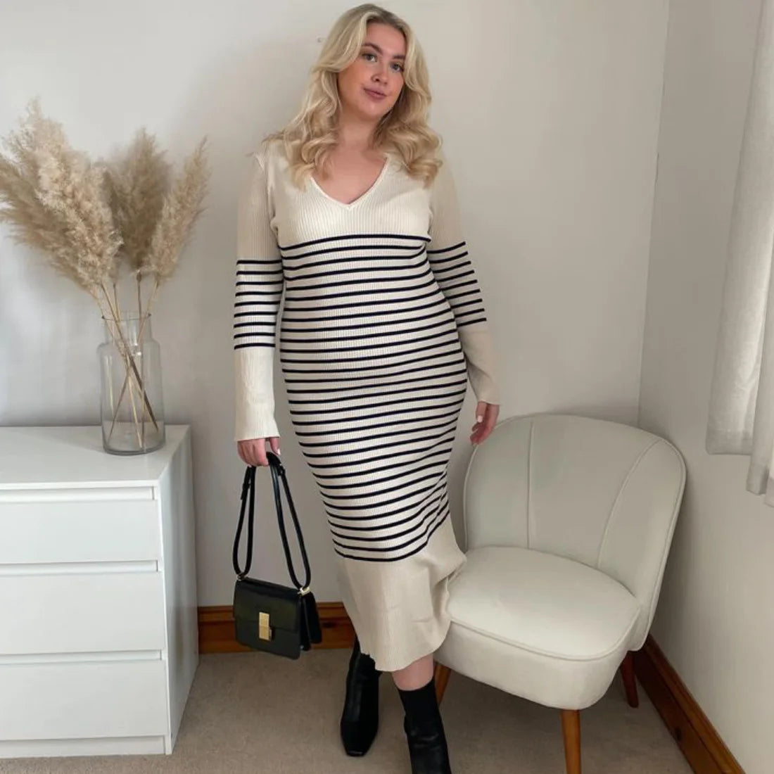 Plus-size woman wearing a long-sleeved striped maxi dress, black boots, and a black handbag