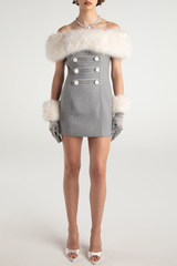 Full-body view of a woman wearing a grey off-the-shoulder mini dress with white faux fur trim and cuffs, grey gloves, and a diamond necklace, standing against a white background.
