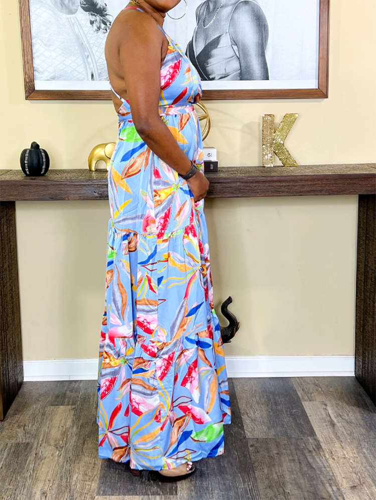Side view of a woman wearing a light blue maxi dress with a tropical floral print, highlighting the flowing silhouette and tiered skirt.