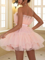 Rear view of a woman in a short, strapless, tiered pink tulle dress with ruffled detailing and a satin bow at the waist.