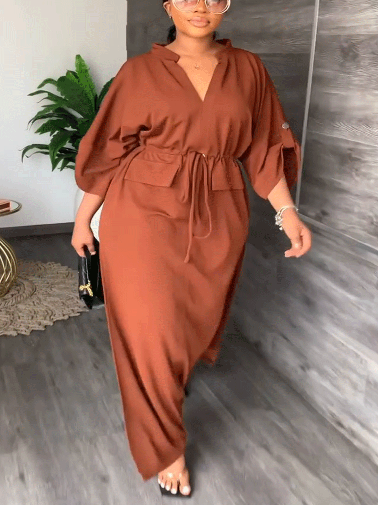 Woman wearing a long rust-colored dress with a v-neck, drawstring waist, and side slits.