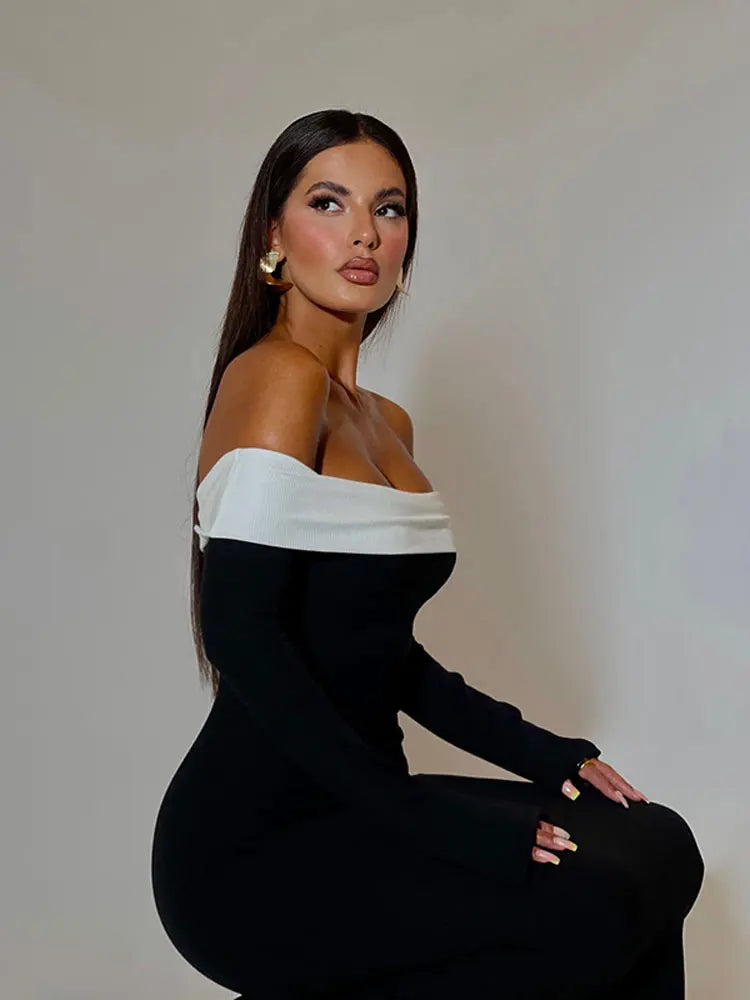 Woman sitting and posing in a black off-the-shoulder floor-length dress with a white trim.