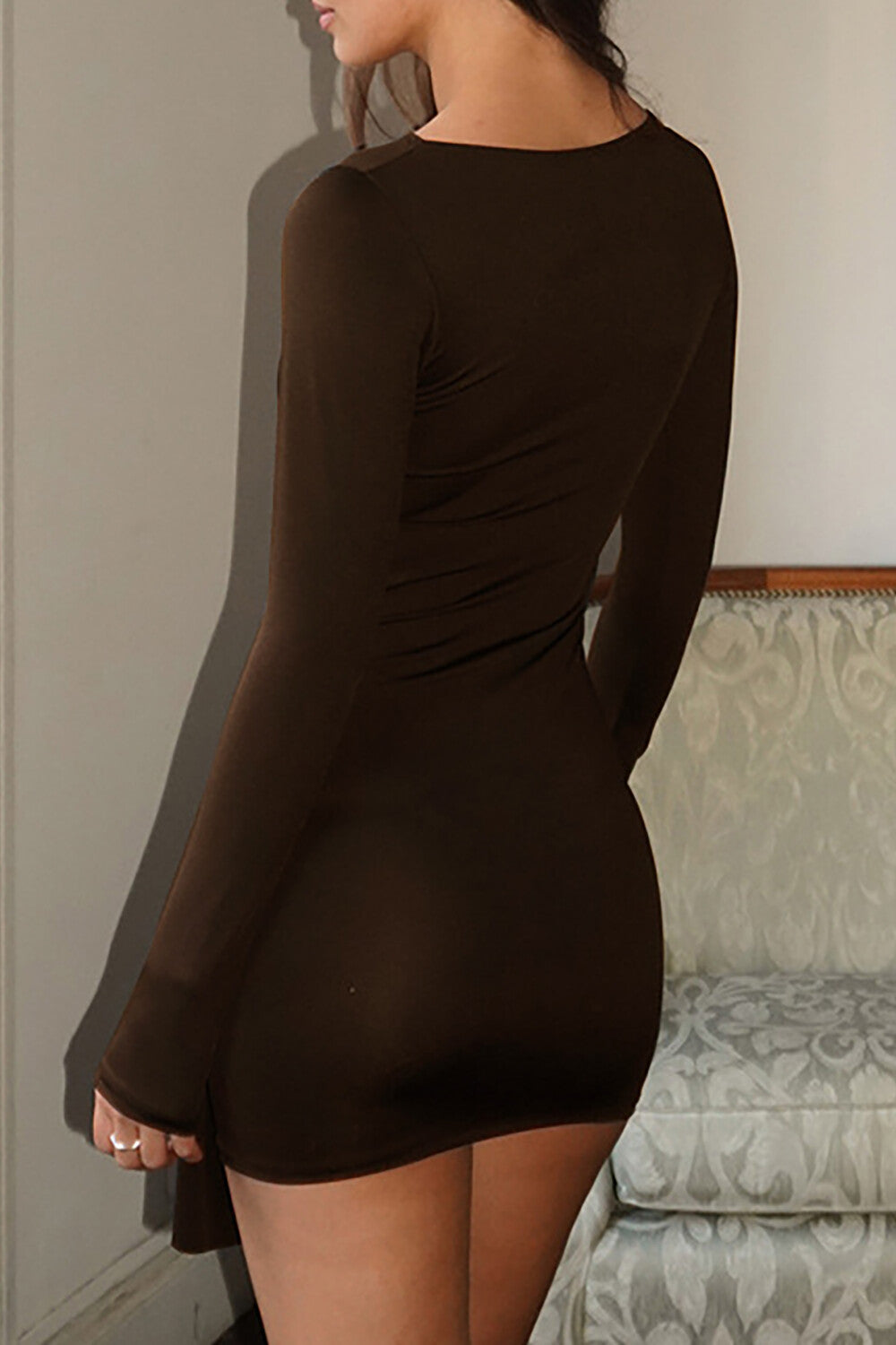 Back view of a woman wearing a brown long-sleeve mini dress with a bodycon fit.