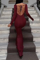 Back view of a woman in a burgundy long-sleeved mermaid dress with a low back, walking up a staircase.