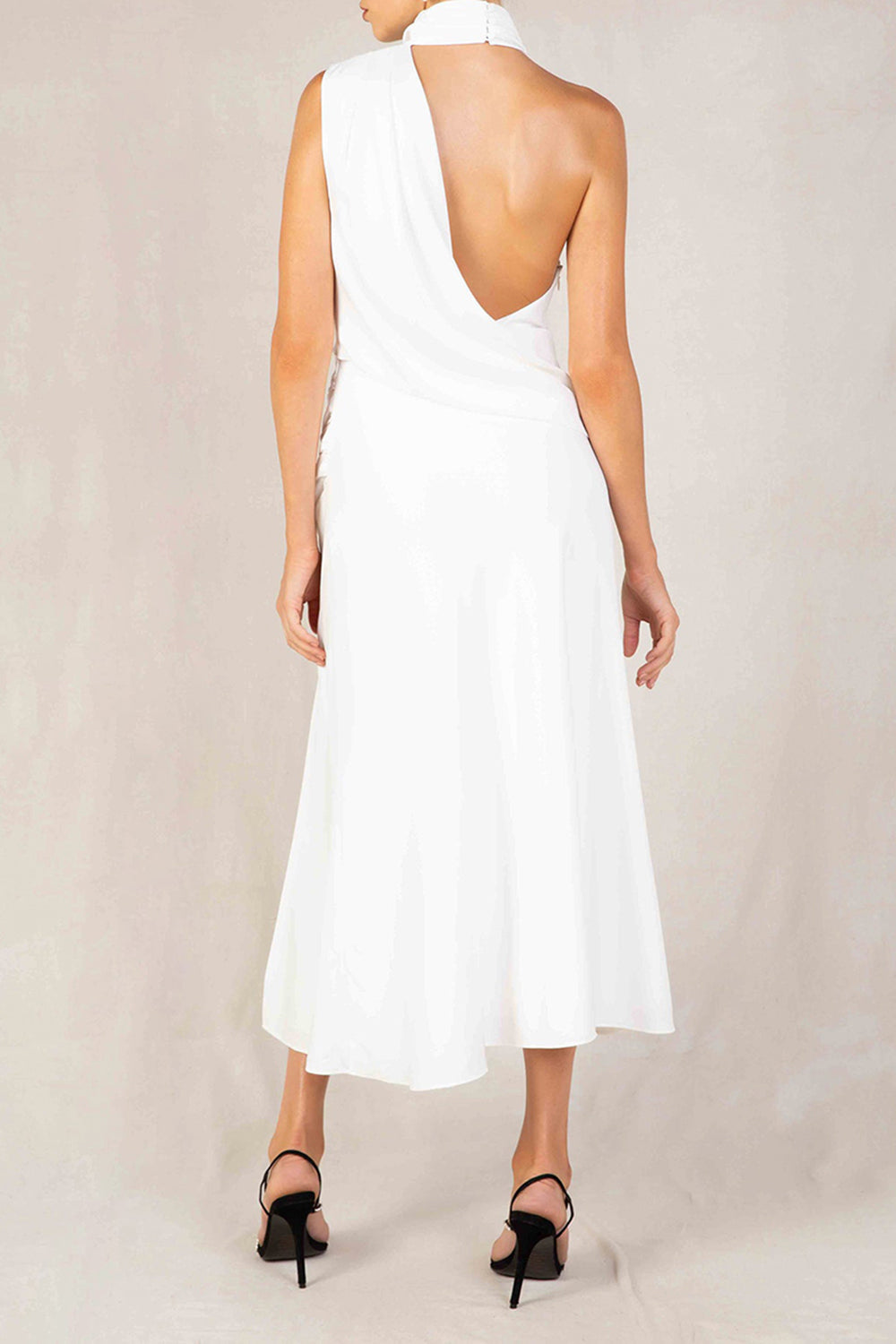 Back view of a woman in a white satin halter neck midi dress with an open back and a thigh-high slit.