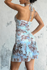 Back view of a woman wearing a blue and brown abstract print halter mini dress, showcasing the ruched back and halter tie.