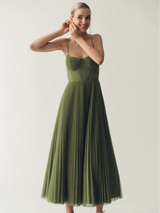 Woman wearing a green pleated midi dress with spaghetti straps and a sweetheart neckline, smiling and adjusting her earrings.