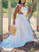 Woman in a white two-piece maxi dress with a halter neckline and ruffled trim, holding a straw bag.