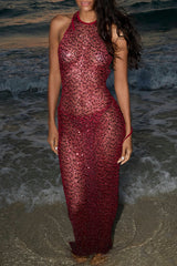 model wearing a long, sheer, red sequined halter dress standing on a beach at sunset