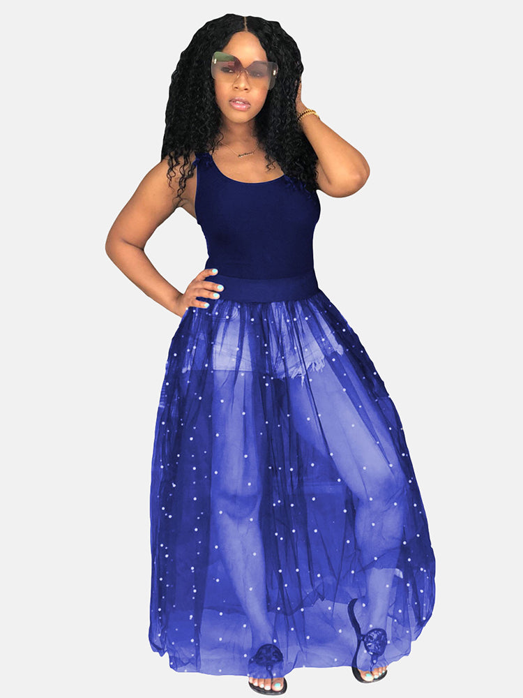 Woman wearing a navy tank top and a navy sheer maxi skirt with white pearl embellishments over denim shorts.