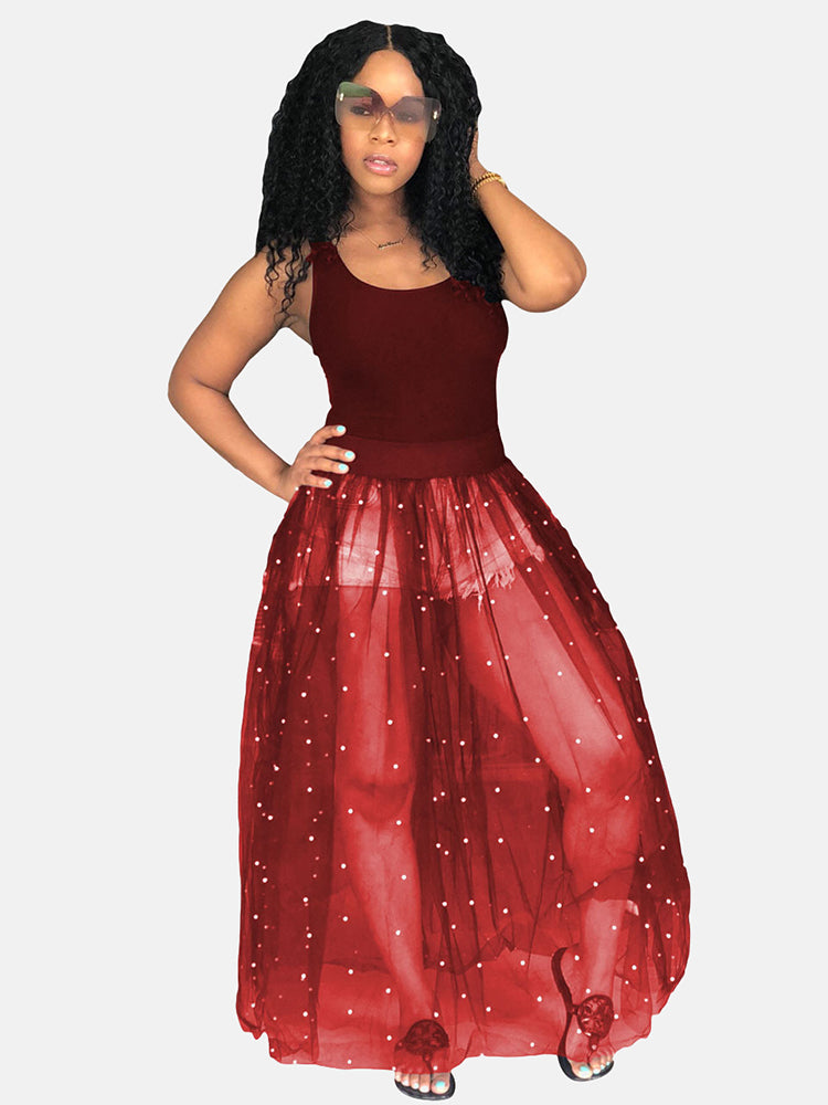 Woman wearing a burgundy tank top and a burgundy sheer maxi skirt with white pearl embellishments over denim shorts.