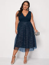 Woman wearing a navy blue sleeveless V-neck midi dress with sparkly embellishments and a tulle overlay, paired with silver heels and a clutch.