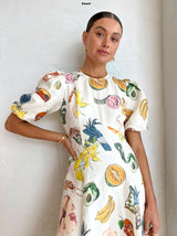 Close-up of a woman wearing a white midi dress with a detailed tropical print, highlighting the puff sleeves and the neckline.