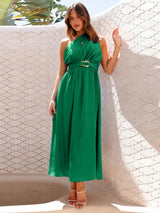 Woman wearing a green one-shoulder midi dress with a belted waist, standing outdoors leaning against a textured wall.