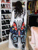 Back view of a woman wearing a white maxi dress with a large, colorful butterfly print on the skirt, standing in front of a closet filled with clothes.