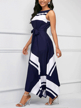 Woman wearing a navy blue and white sleeveless A-line maxi dress with a scoop neck, tie waist, and asymmetrical hemline, side view