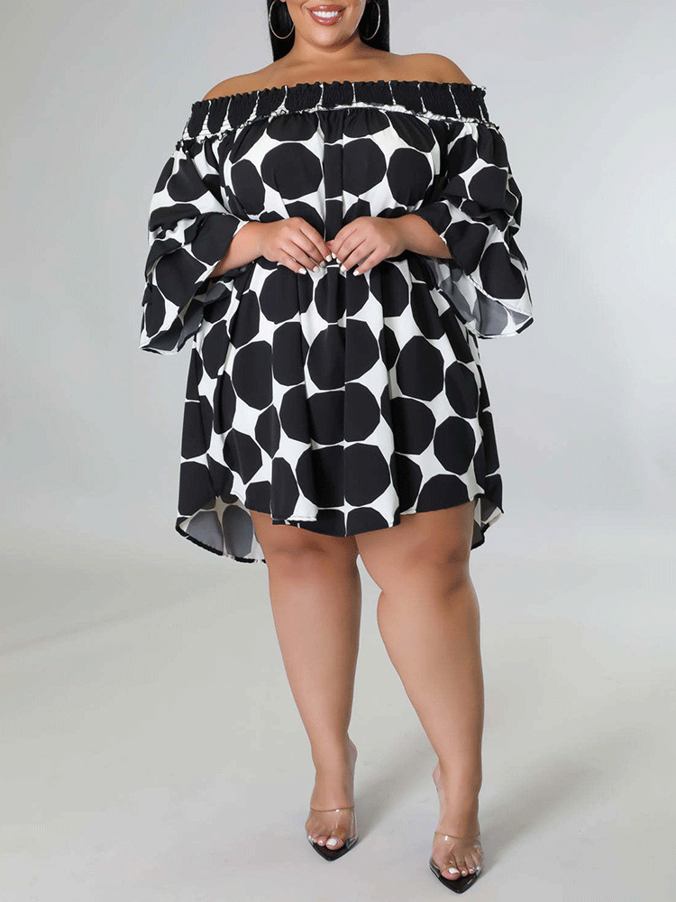 Full body shot of a woman in a black and white polka dot off-the-shoulder dress.