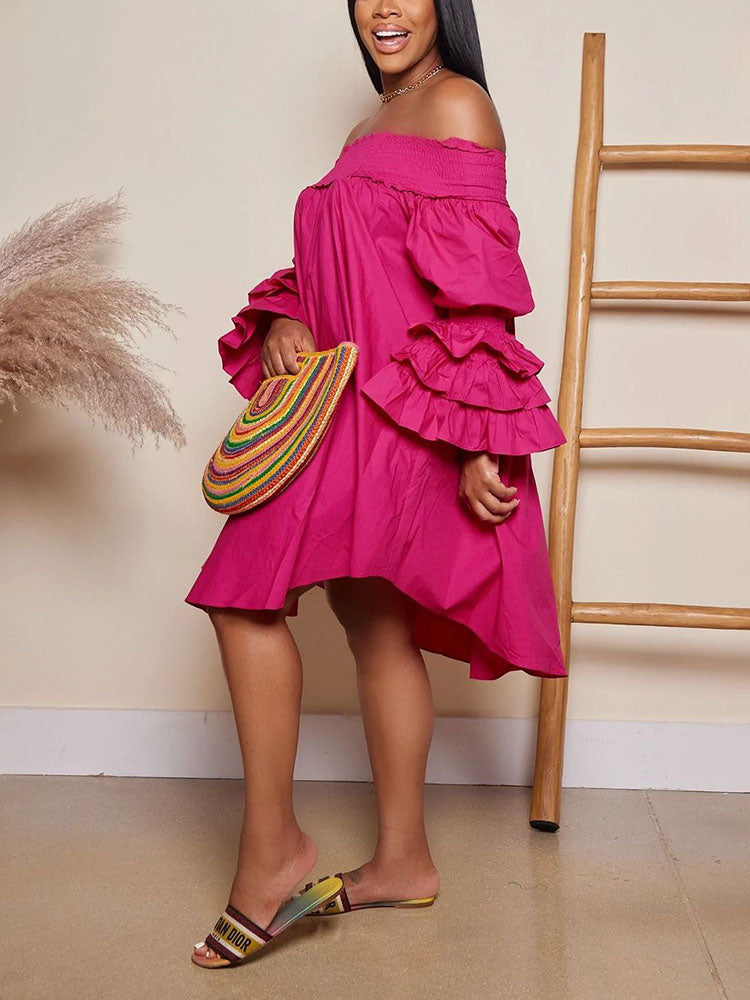 Woman wearing a bright pink off-the-shoulder dress with tiered ruffled sleeves and a high-low hemline, holding a colorful clutch and wearing colorful slides.