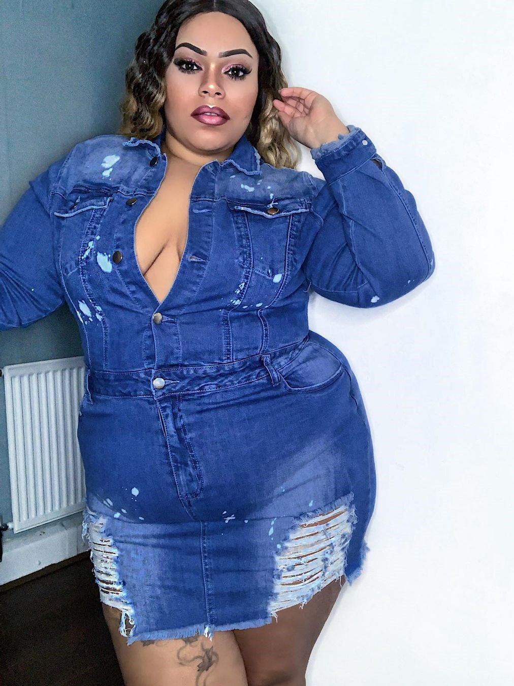 Close-up of a plus-size model wearing a distressed denim mini dress with paint splatter, emphasizing the neckline and texture.