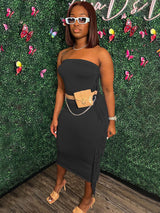 Woman wearing a black strapless midi dress with fringe trim and a beige fanny pack, paired with beige heels.