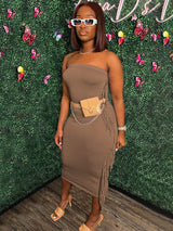 Woman wearing a brown strapless midi dress with fringe trim and a beige fanny pack, paired with beige heels.