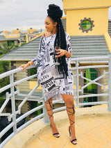 Woman wearing a black and white newspaper print t-shirt dress with black strappy heels, standing on a balcony.