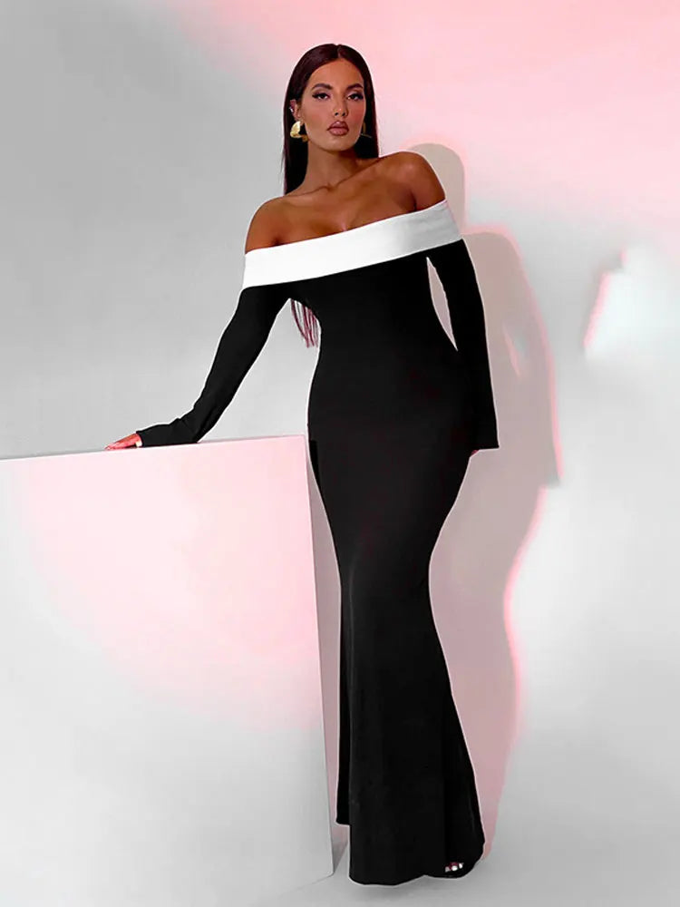 Woman in a black off-the-shoulder floor-length dress with a white trim, leaning on a white surface with pink lighting.