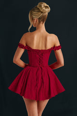 Back view of a woman wearing a red off-the-shoulder mini dress with a ruffled neckline and corset bodice, showing the lace-up detail.