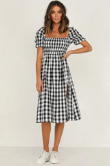 Woman wearing a black and white gingham check midi dress with puff sleeves and a square neckline, standing with her hand on her hip.