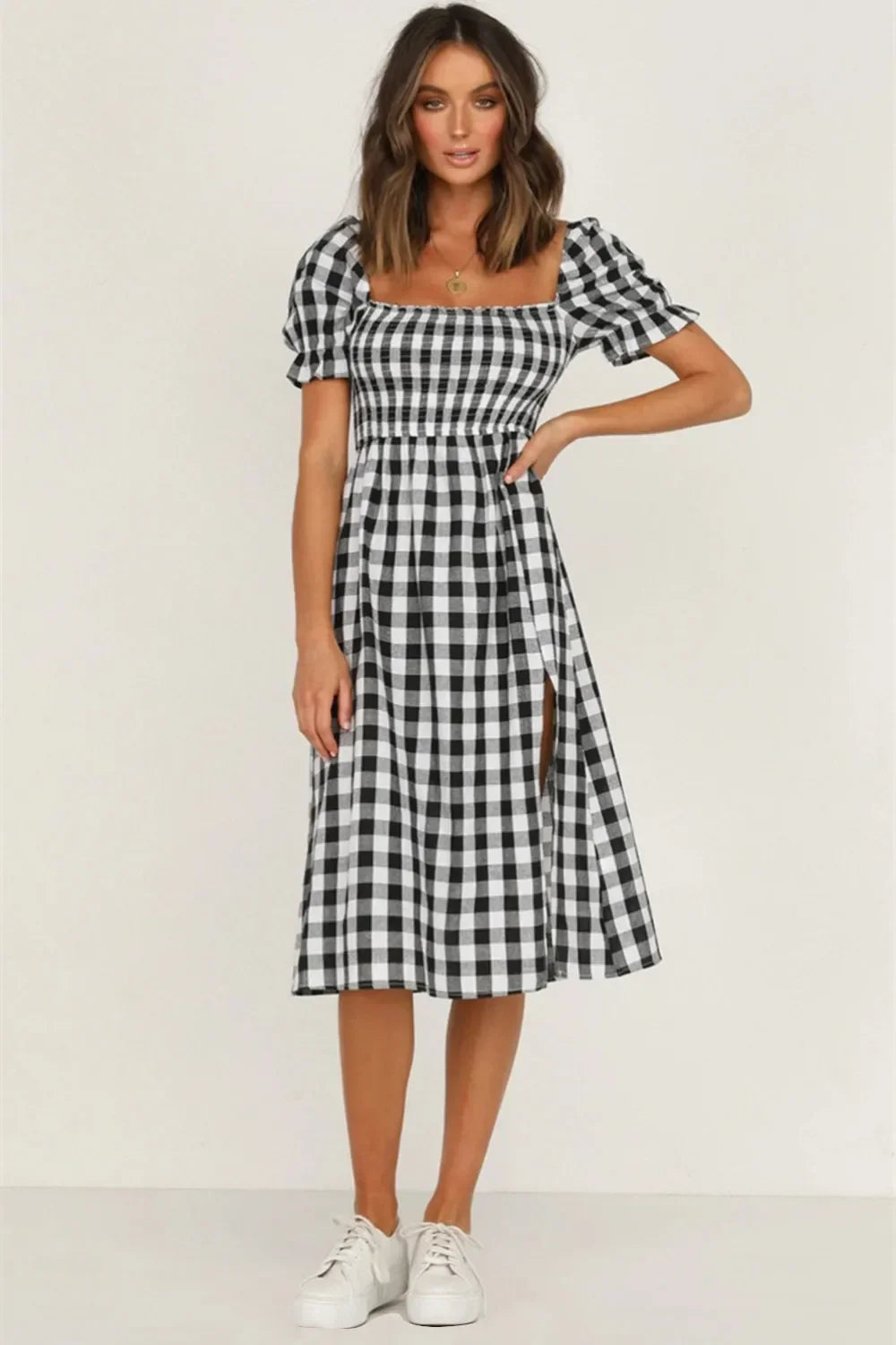 Woman wearing a black and white gingham check midi dress with puff sleeves and a square neckline, standing with her hand on her hip.