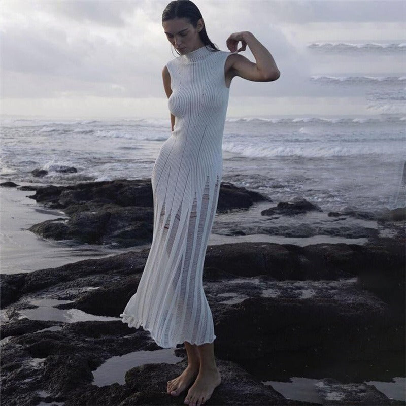 Woman wearing a white sleeveless ribbed knit midi dress with sheer panel detailing posing on rocks by the ocean