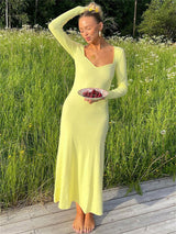 Woman in a yellow ribbed knit maxi dress with long sleeves and a sweetheart neckline holding a small plate of cherries in a grassy field.