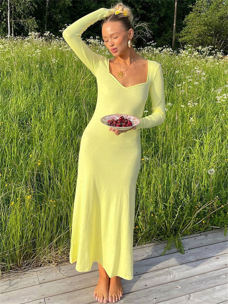 Woman in a yellow ribbed knit maxi dress with long sleeves and a sweetheart neckline holding a small plate of cherries in a grassy field.